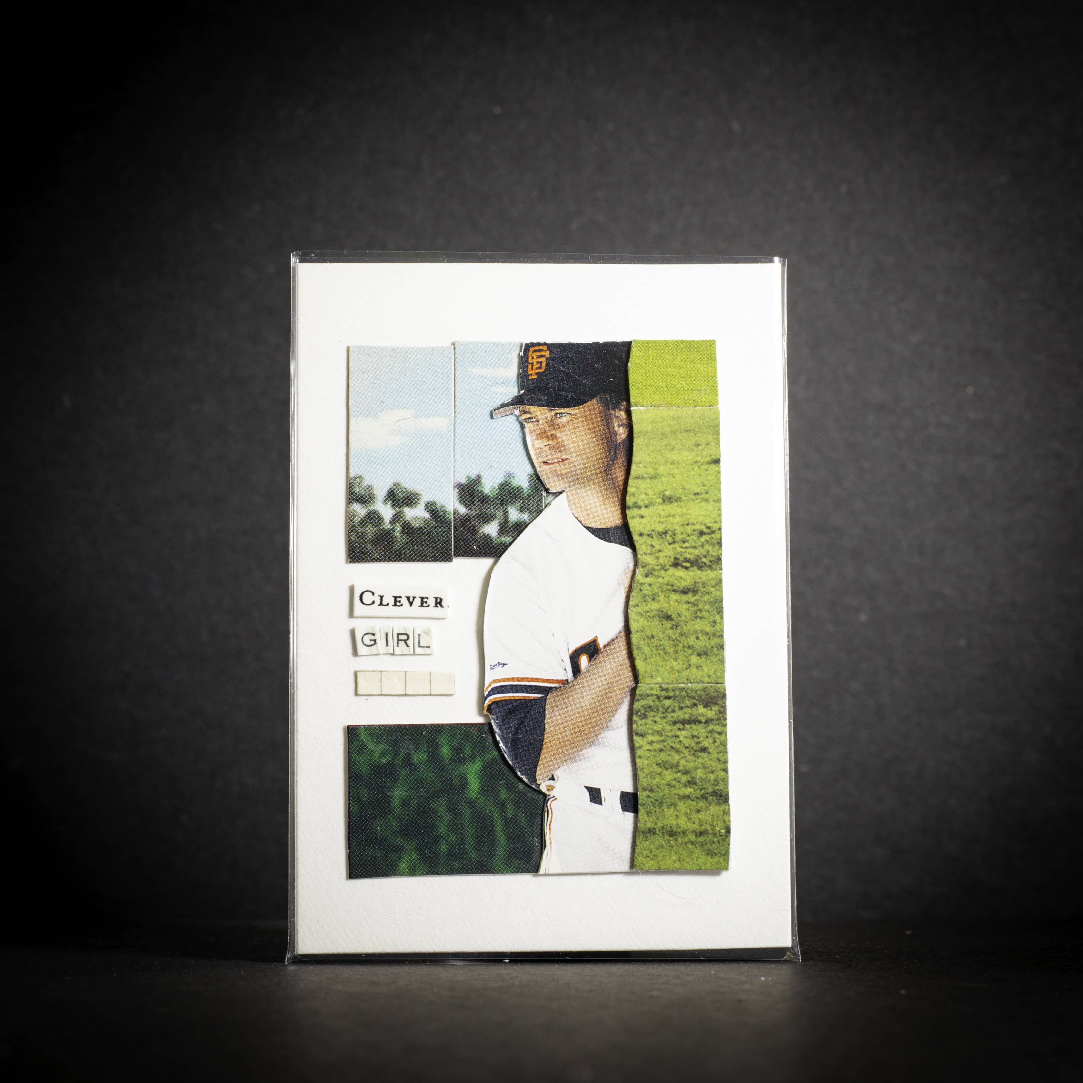 Baseball card of a player in a white uniform with a dark cap on a dark background